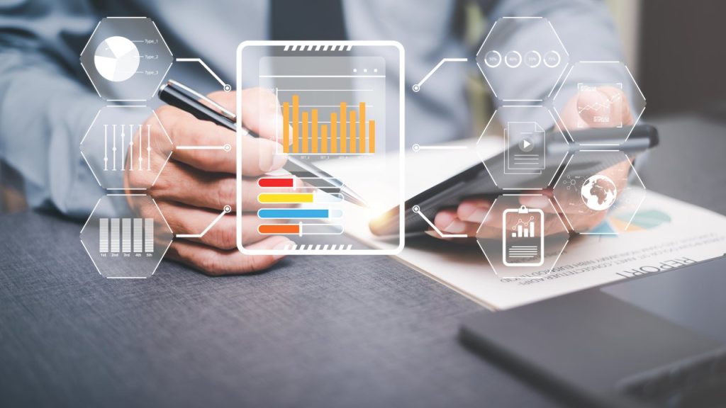 Persona usando un lápiz y un dispositivo móvil sobre un escritorio, con gráficos digitales superpuestos que muestran datos, estadísticas y análisis en tiempo real.