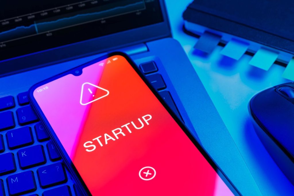 Smartphone con app de startup sobre laptop y entorno de trabajo digital.